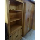 A modern pine bookshelf with cupboard base together with a modern lightwood triple wardrobe and a