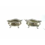 PAIR OF SILVER SALTS & MATCHING SPOONS of oval form on four pad feet and with feathered decorative