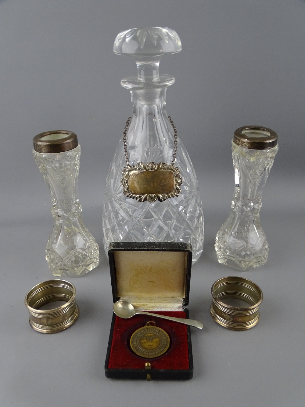 MALLET FORM CUT GLASS DECANTER WITH STOPPER bearing a blank silver label, two napkin rings and two