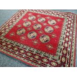 100% WOOL RED GROUND WILTON RUG with decorative nine medallion centre and geometric border, 274cms