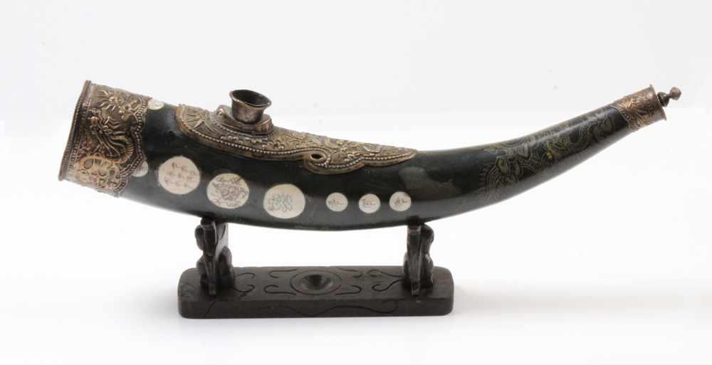 Opium-Pfeife.China, 19. Jh. Graviertes und beschlagenes Horn, Beineinlagen. Holzständer. L: 41 cm.