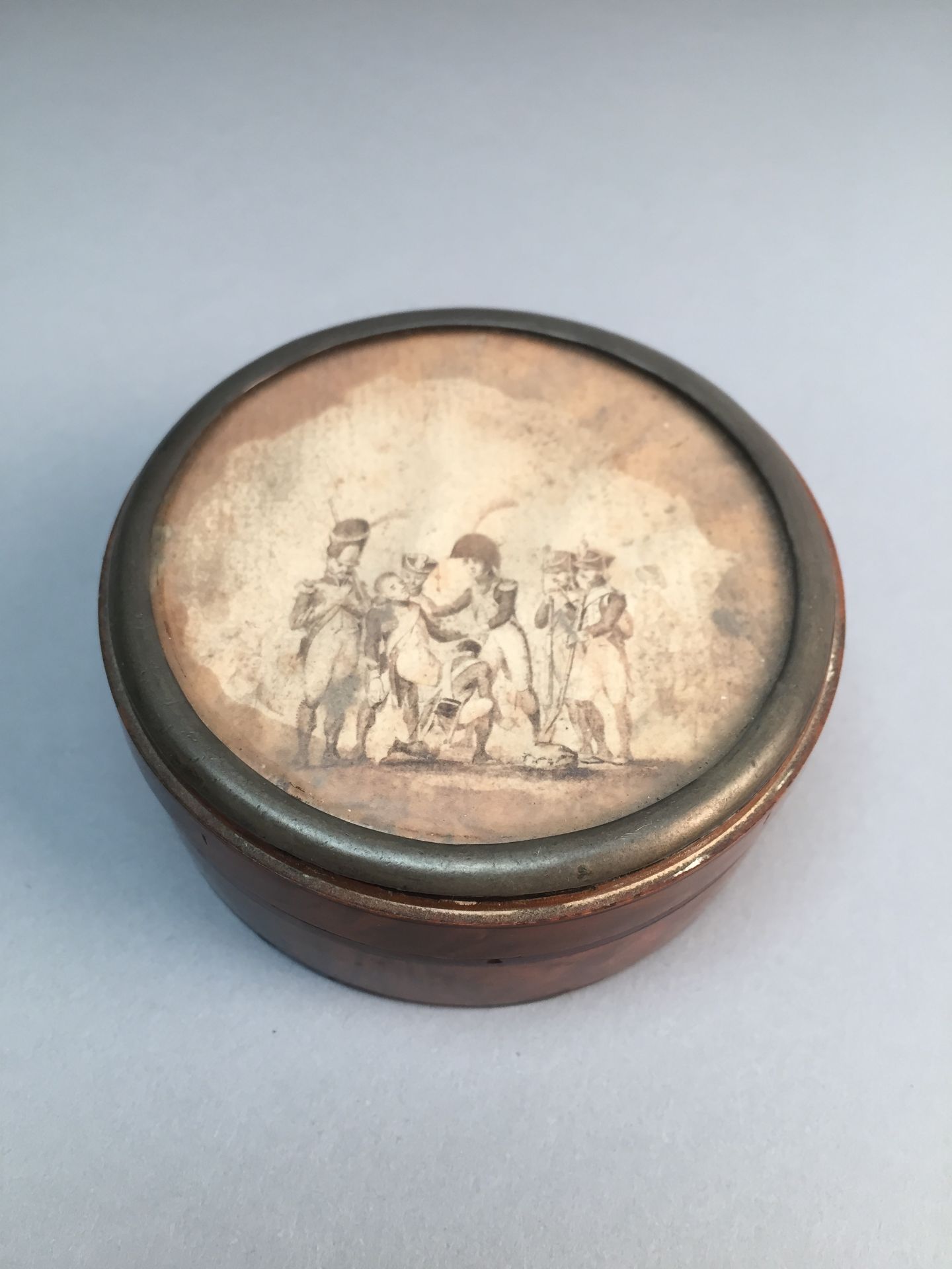 Boite ronde en loupe et écaille. A décor d'une scène militaire. D : 8 cm. Accidents. -