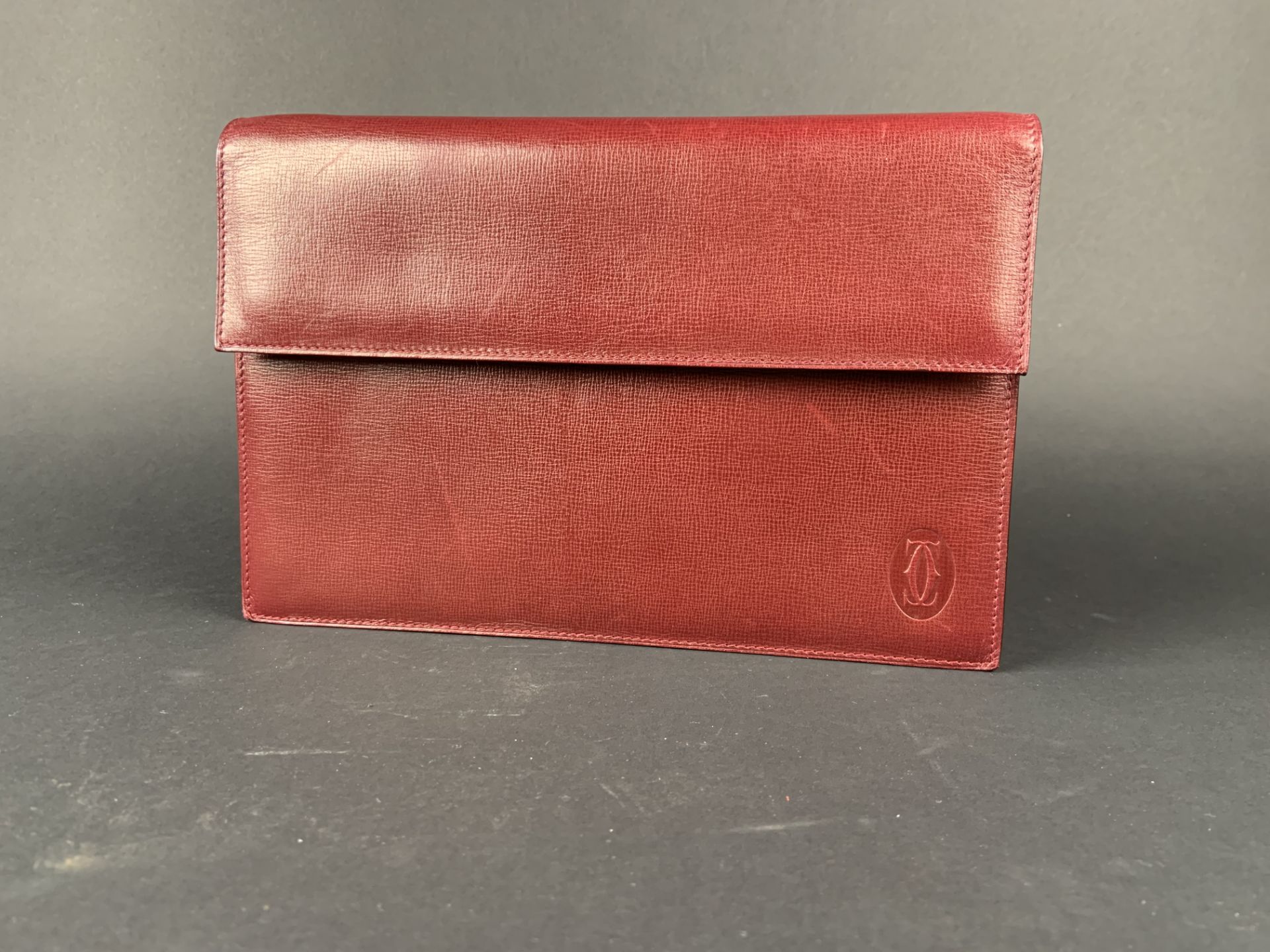 CARTIER. Pochette en cuir bordeaux fermé par une pression. Dustbag. -