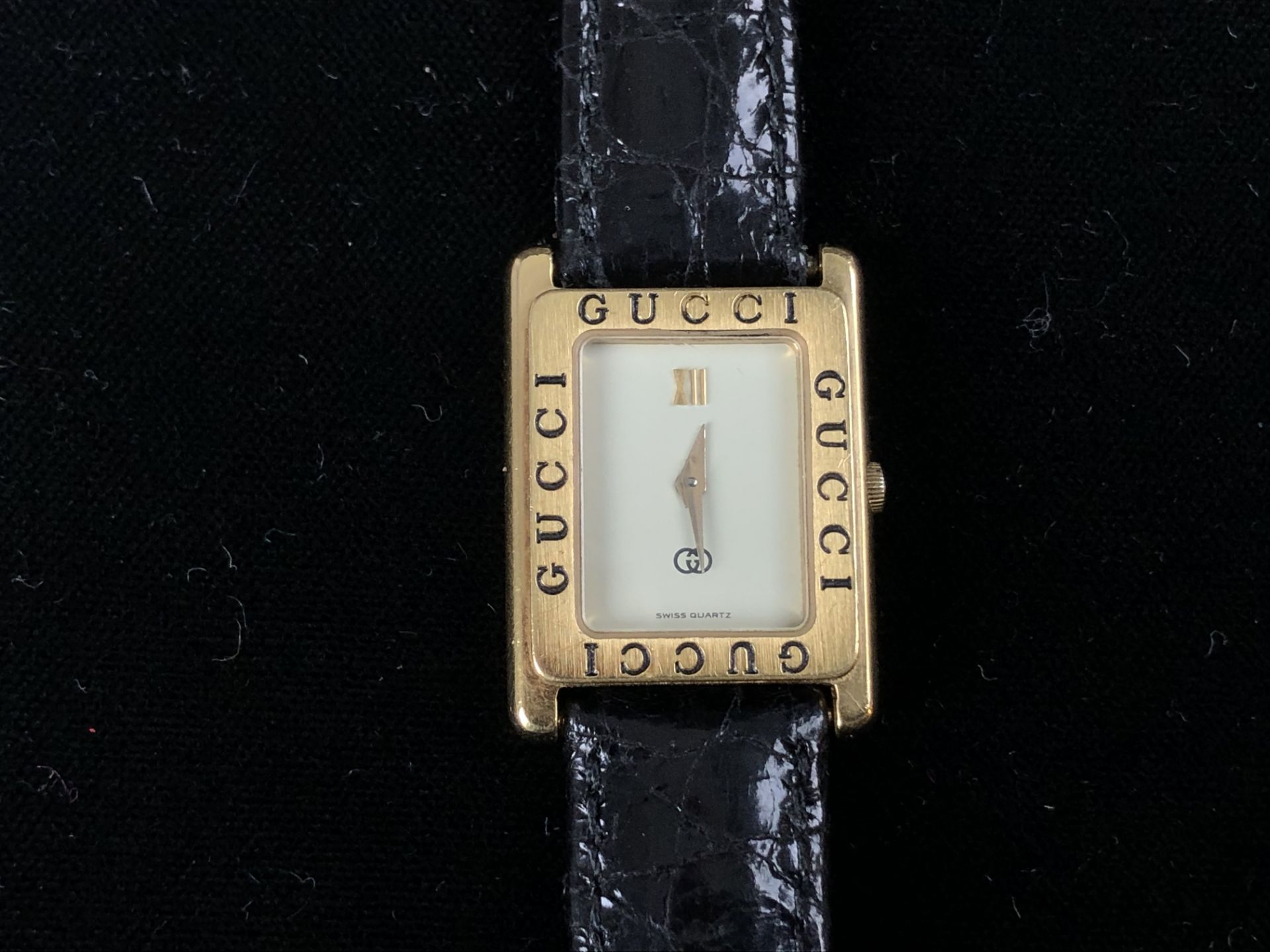 GUCCI. montre de dame carrée dorée, bracelet cuir vernis noir. -