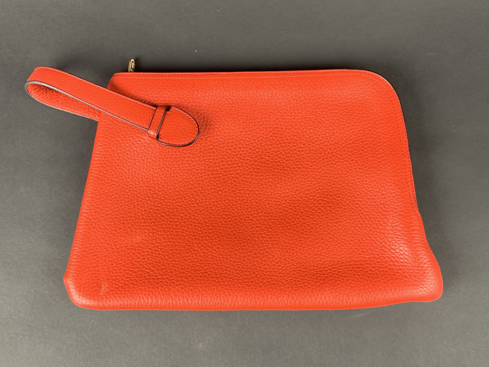 DELVAUX. Pochette porté main, cuir grainé rouge avec une anse. -