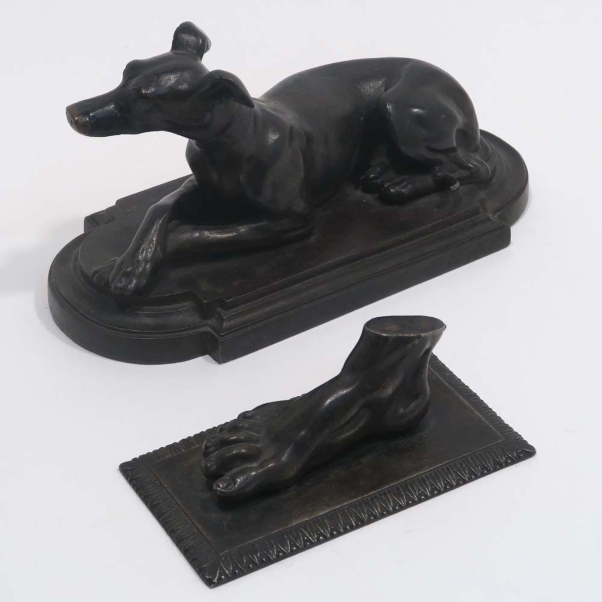 Liegender Hund / FußBronze, braun patiniert. 9 x 18 x 8 cm bzw. 4 x 10,5 x 5,5 cm.