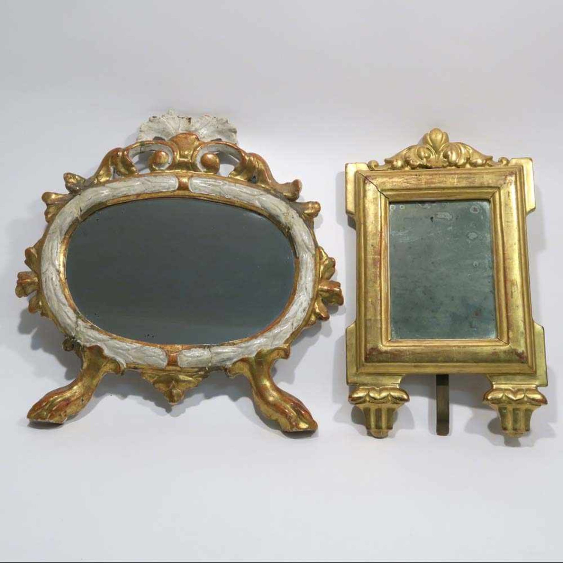 Zwei SpiegelHolz, beschnitzt, gold bzw. weiß gefasst. Hochrechteckig bzw. ovale Form auf Füßen. Tlw.