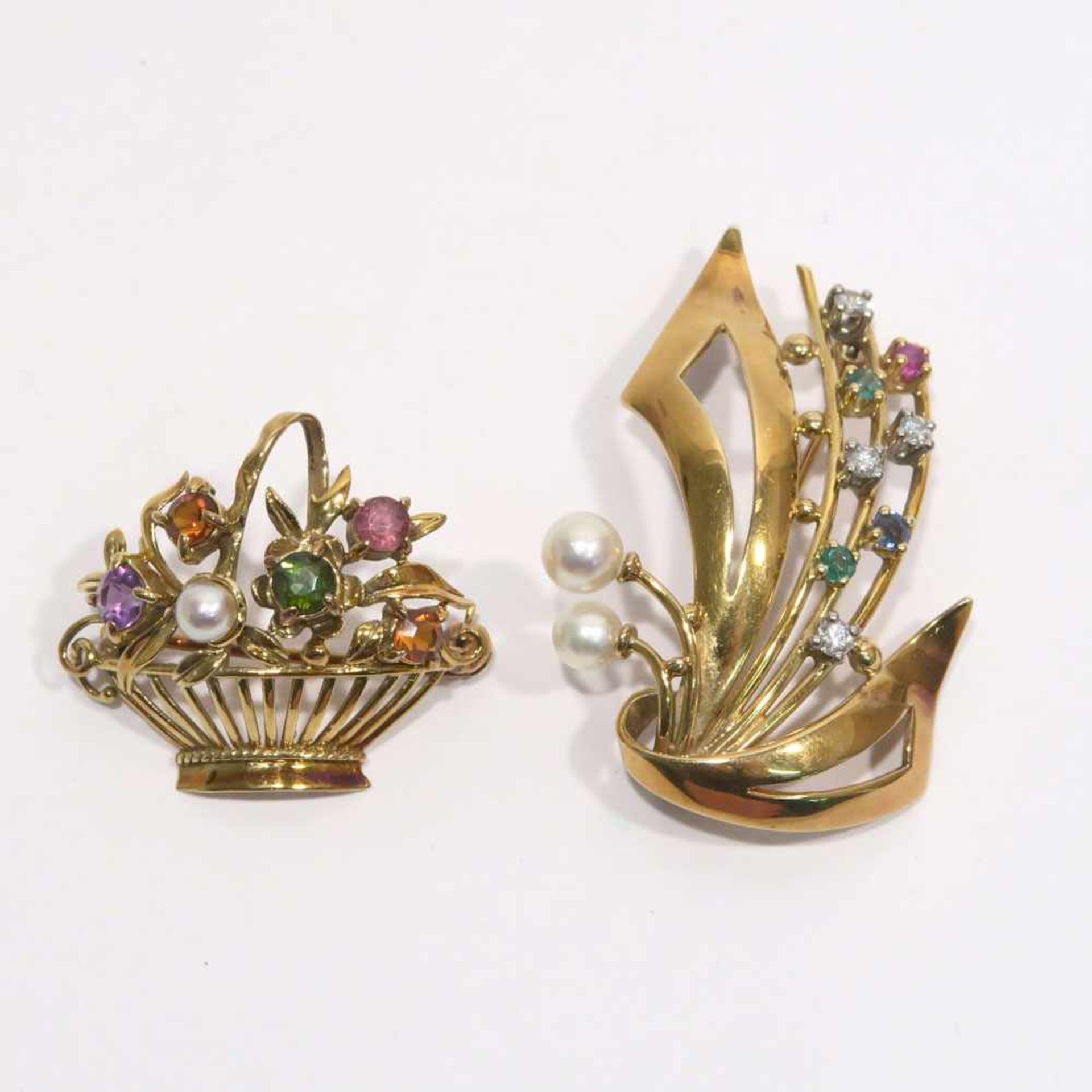 Zwei Broschen14 K GG, Marken (585). Mit zwei Perlen, einem Saphir, einem Rubin, zwei Smaragden und