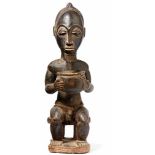 Cult figure of SenufoWest Africa, Côte d'IvoireSitting on stool, holding vessels for ritual
