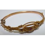 An Edwardian 9ct gold bangle, the panel front set with red paste and diamond chips, weight 5.5 gms.