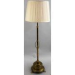 A brass adjustable standard lamp, the column supported on a circular base with ribbon and swag