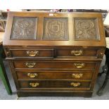 An oak bureau the fall front with carved coat of arms flanked by rose head, fitted interior, over