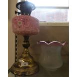 A brass oil lamp with pink glass bowl and etched glass shade