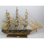 A wooden model of an 18th century three-masted frigate, raised on a wooden plinth with plaque that