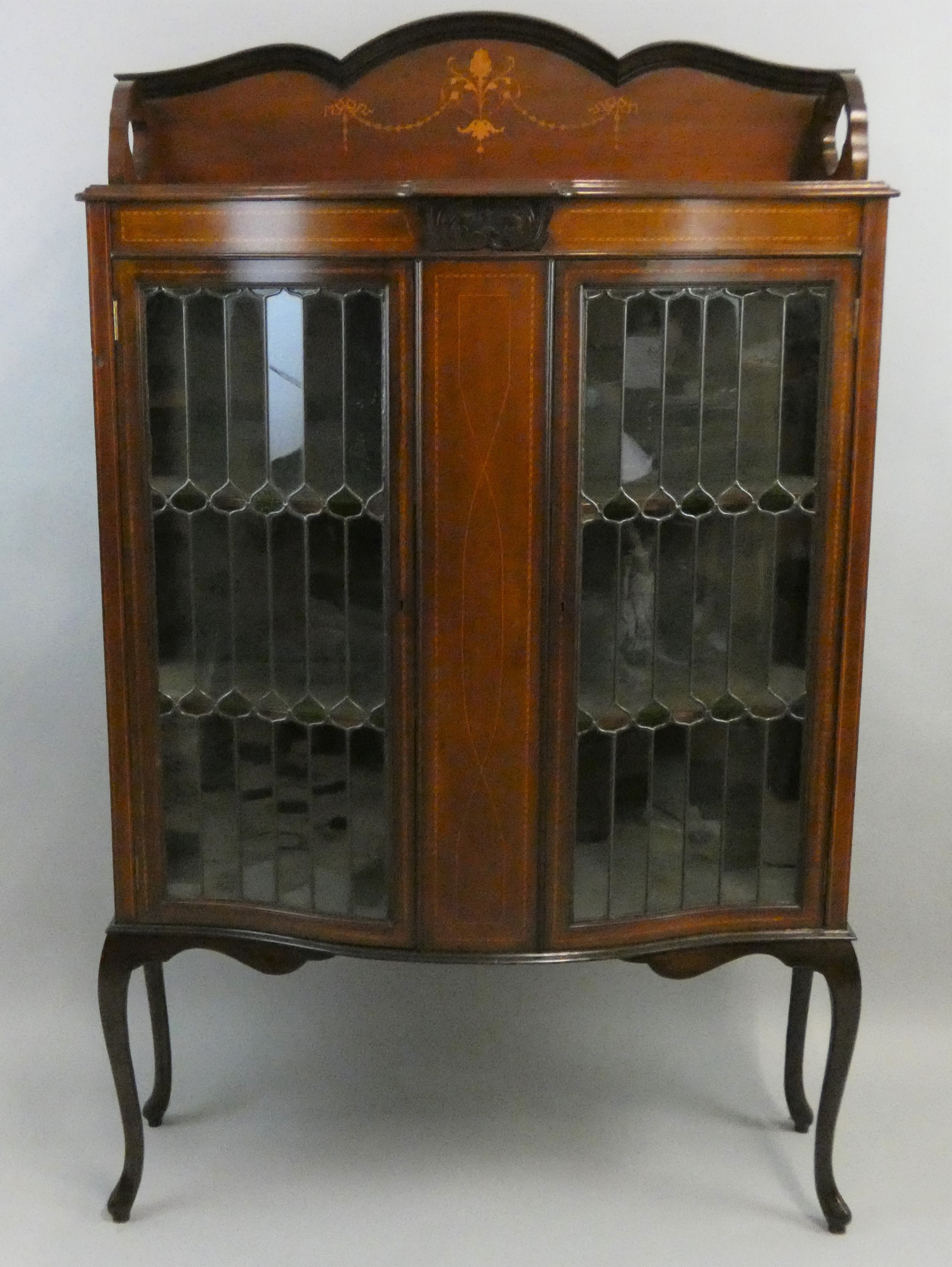 An Edwardian mahogany display cabinet, the bowed stylised leaded glass doors, with boxwood inlaid
