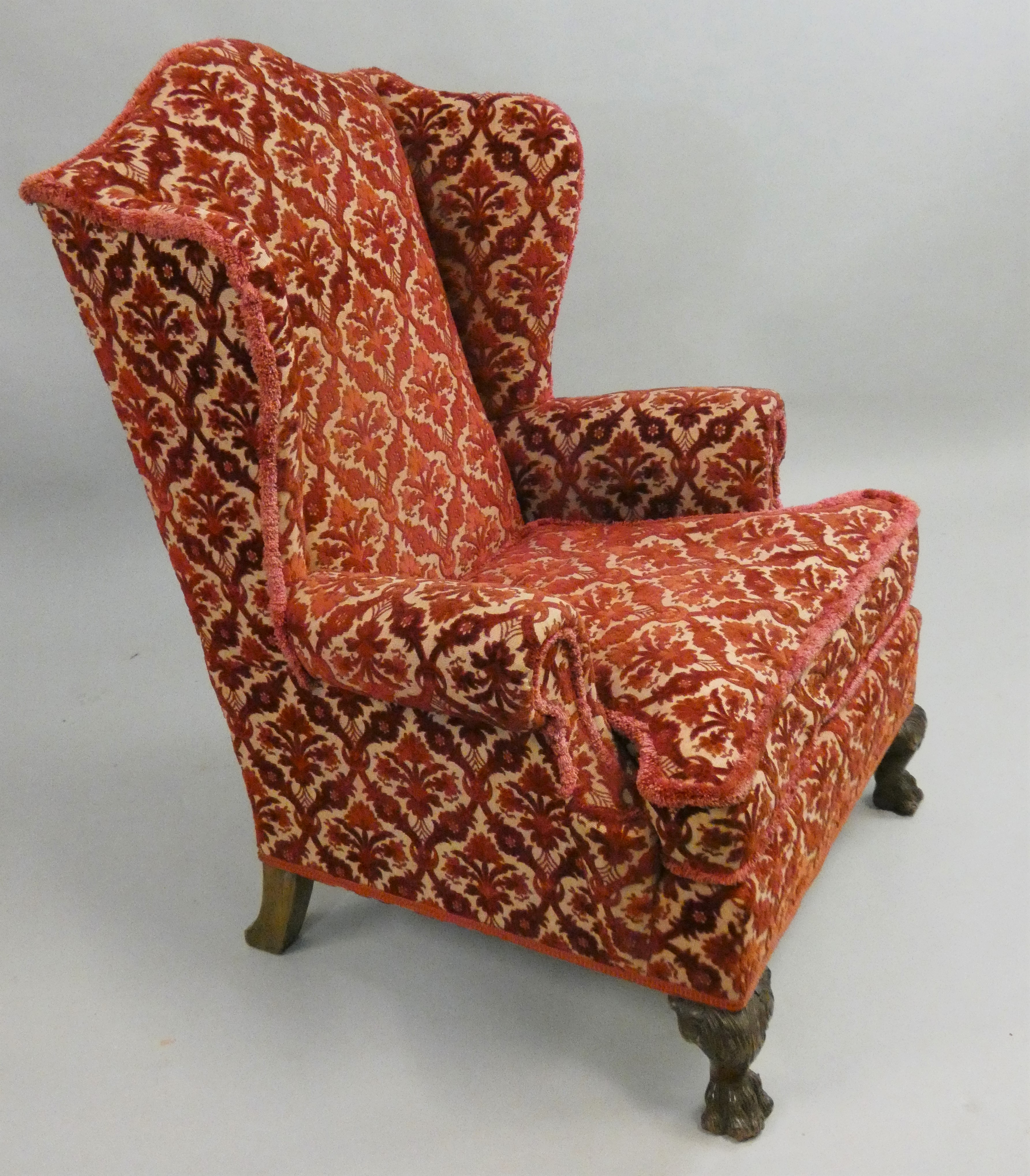 An upholstered wing armchair, raised on hairy lions paw feet, 82 cm wide.