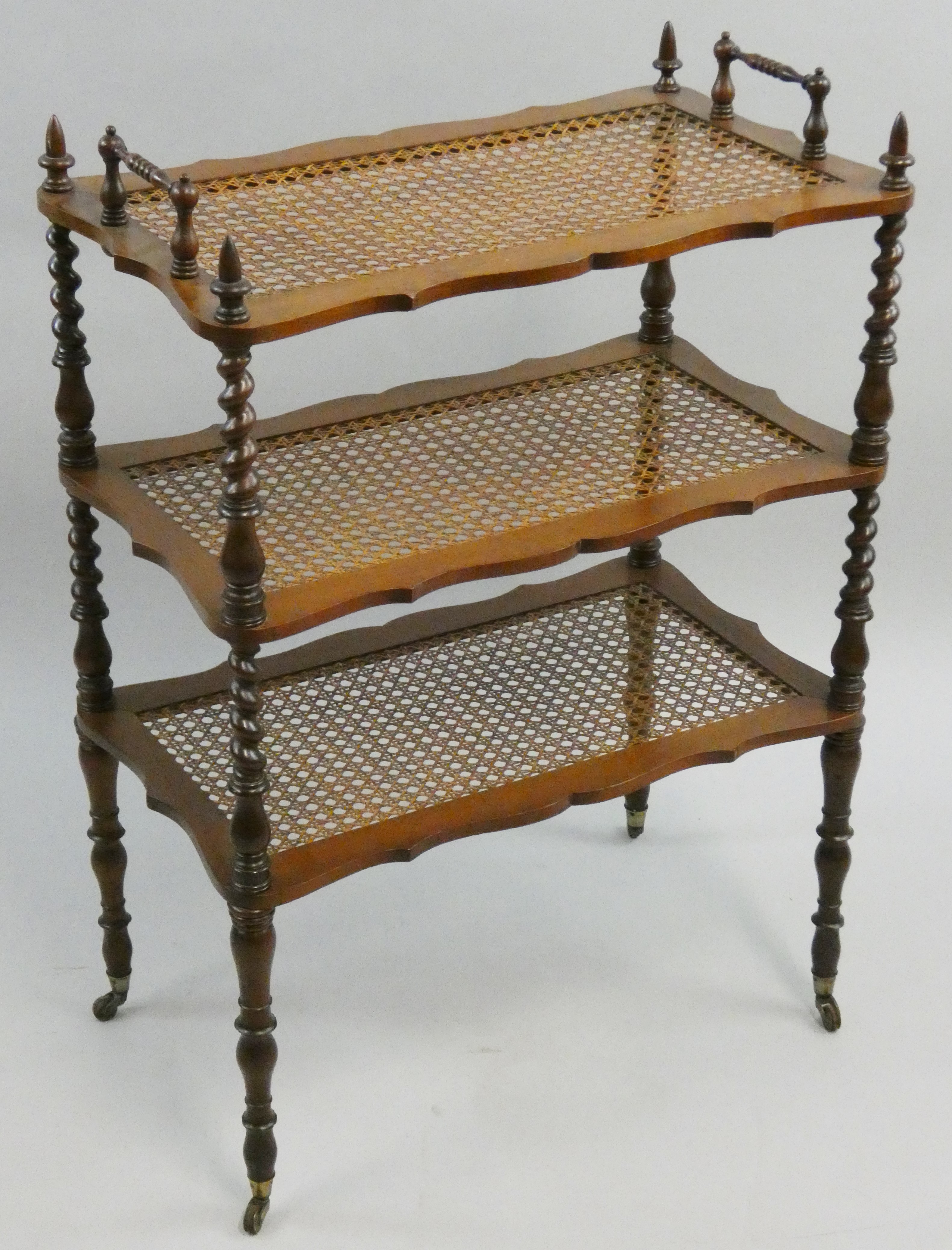 An Edwardian mahogany and cane three tier trolley, with turned supports between, raised on brass