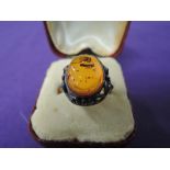 A lady's dress ring having an oval Baltic amber stone in a decorative moulded mount on a white metal