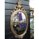 An oval hall way mirror with elaborate gilt effect frame