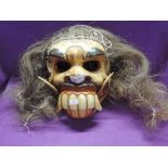 A hand carved and decorated wooden mask with faux hair and movable jaw