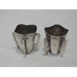 A pair of Edwardian Irish silver whisky tots of Arts and Crafts form having applied strap handles,