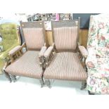 A pair of late Victorian oak salon armchairs having foliate carved frieze and later striped