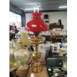 A tall standing brass bodied oil burning lamp with red shade