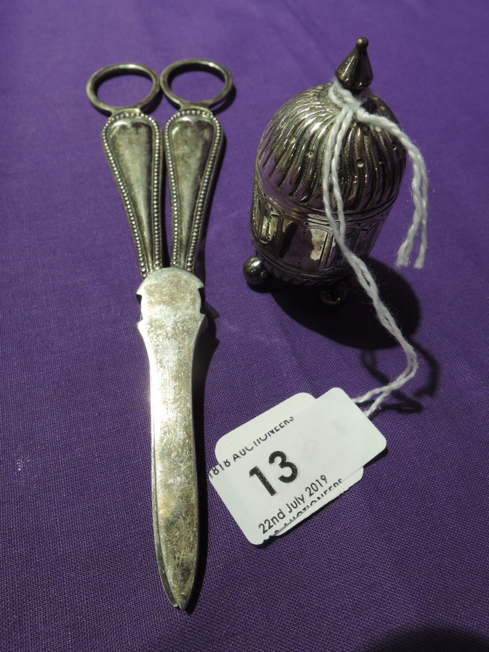 A small white metal pepperette having continental style decoration and trefoil bun feet, no marks