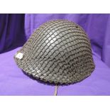 A metal military helmet covered in netting, very good condition