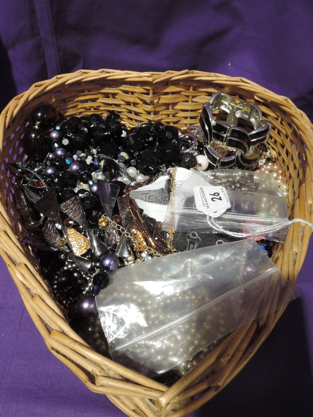 A basket containing a selection of costume jewellery including diamante necklaces, watches, earrings