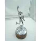 A chrome car mascot mounted on a wooden base depicting Greek god Hermes holding the staff of