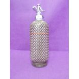 A vintage soda syphon with metal basket weave cover