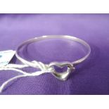A white metal tension bangle stamped 800 having a heart shaped clasp with diamond chip decoration