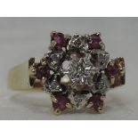 A lady's dress ring having a stylised diamond and ruby chip cluster to butt shoulders on a 9ct