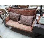 An Edwardian stained frame settee having burgundy and gold embossed upholstery, on leaf carved frame