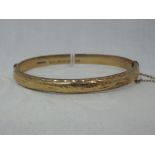 A 9ct gold hinged bangle having engraved scroll decoration