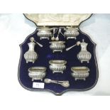 An cased Edwardian silver eight piece condiment set having gadrooned decoration and bun feet,