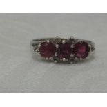 A lady's dress ring having a trio of rubies with diamond chips to shoulders on a 9ct white gold