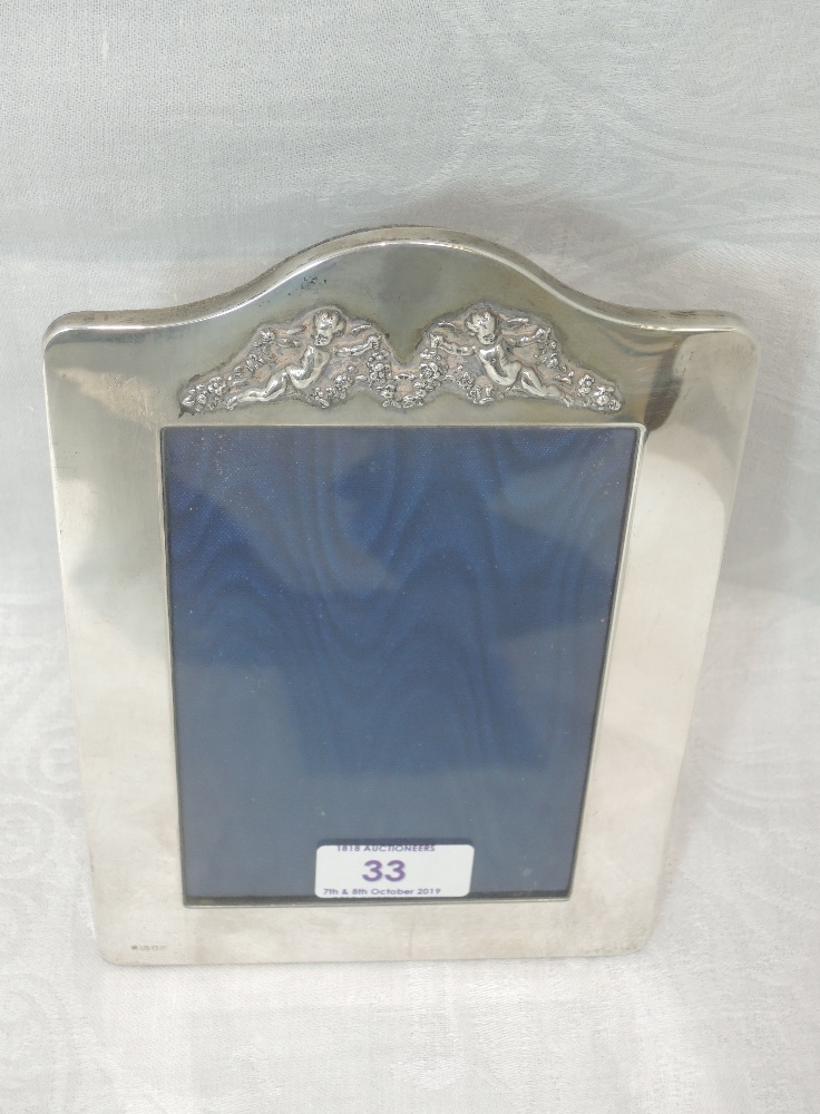 A silver photograph frame of plain arched form having moulded cherub decoration to top and velvet