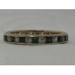 A yellow metal eternity ring stamped 9ct having white and green paste stones in a channel setting,