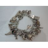 A white metal charm bracelet stamped silver having 25 charms including Concorde, peacock, church,