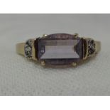 A lady's dress ring having a facetted amethyst style stone flanked by diamond chips in a 9ct gold
