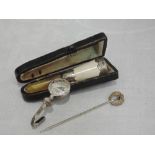 An HM silver napkin clip having engraved decoration, a cased cigarette holder with white metal