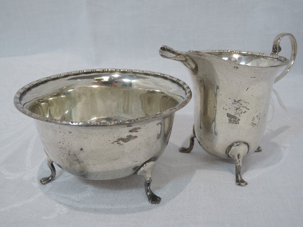 A silver sugar bowl and cream jug of plain form having decorative rims and paw feet, Birmingham