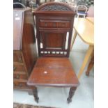 A late Victorian mahogany hall chair having crest spindle and panel back, with solid seat and turned