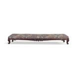 A CARVED MAHOGANY FRAMED LONG STOOL, 19th century, covered in floral fabric with foliate carved