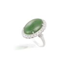 A JADEITE JADE AND DIAMOND RINGThe translucent oval-shaped jadeite jade cabochon of green hue within