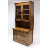 An Ercol elm tall cabinet, the upper part fitted two shelves enclosed by pair of glazed doors