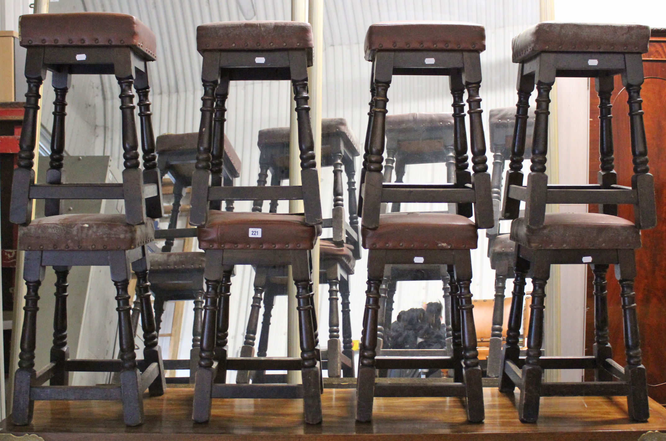 A set of eight bar stools with brass studded brown leatherette seats & on turned legs with plain