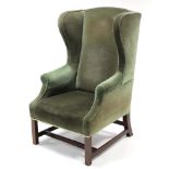 A Georgian-style wing-back armchair, upholstered dark green velour, & on short mahogany legs with